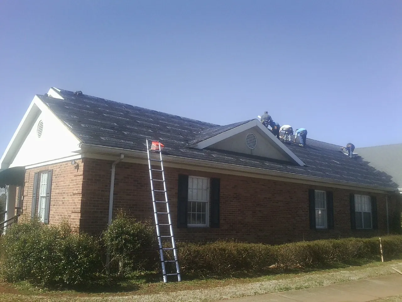Crew tearing shingles off a brick ranch roof with a ladder set — Metal Roof Repair work by our crew in Valleyford