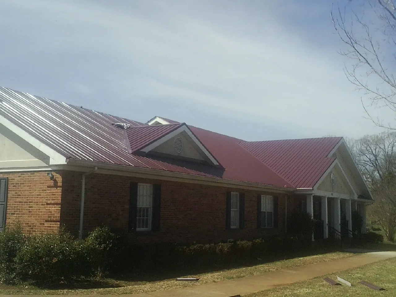 Red metal roof with gabled entries on a long brick building, from a Hail Damage Roof Repair job in Valleyford
