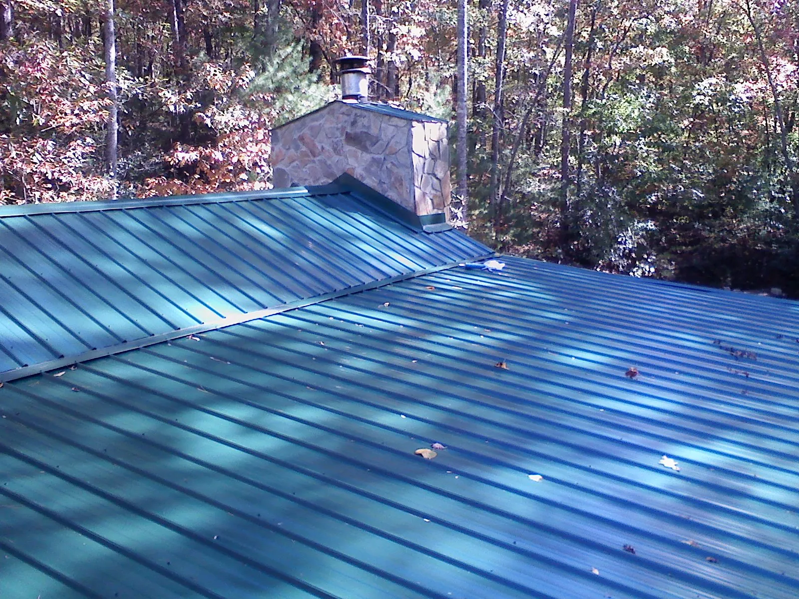New green metal roof and stone chimney surrounded by autumn woods in Valleyford