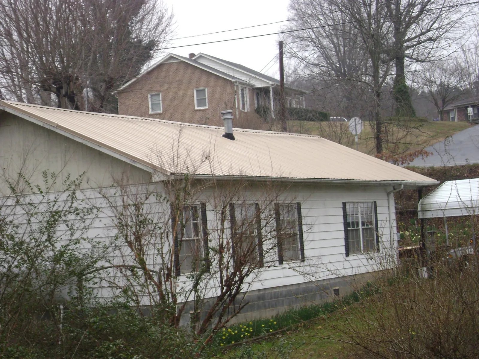 Tan metal roof on a white sided house set into a hillside — Commercial Roofing by Roofing Brothers in Valleyford
